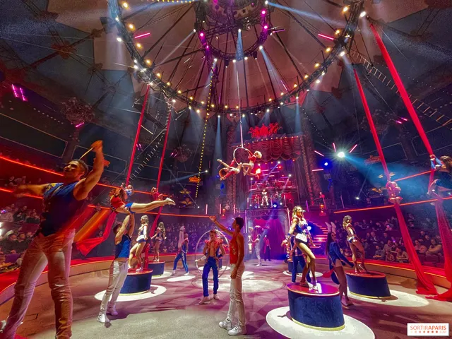 Des artistes de cirque sur des podiums, sous un chapiteau illuminé