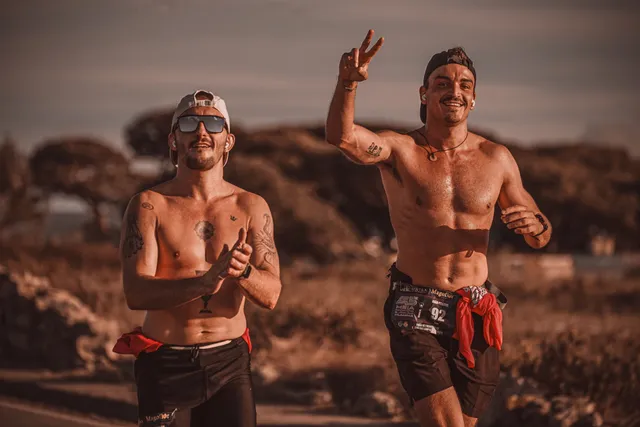 Deux coureurs souriants en pleine course au soleil, l'un fait un signe de la main