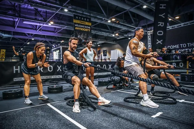 Des athlètes enchaînent des exercices à la corde ondulatoire dans une grande salle