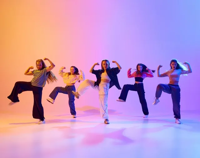 Cinq danseuses en tenue hip-hop prennent la pose sur un fond orange et violet