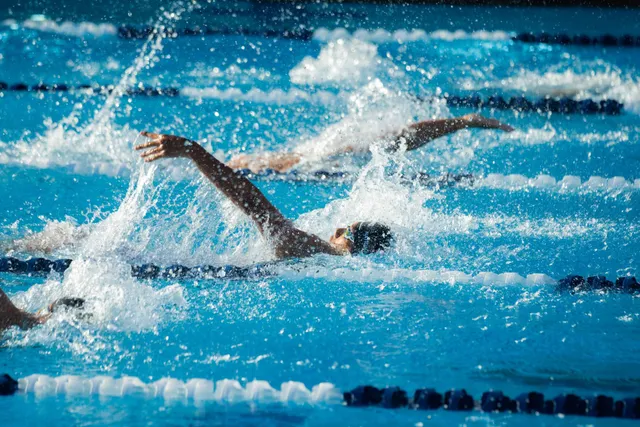 Des nageurs en dos crawlé dans les lignes d'eau d'une piscine, au milieu des éclaboussures