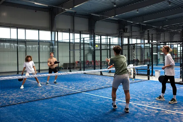 Quatre joueurs en plein échange sur un terrain de padel couvert