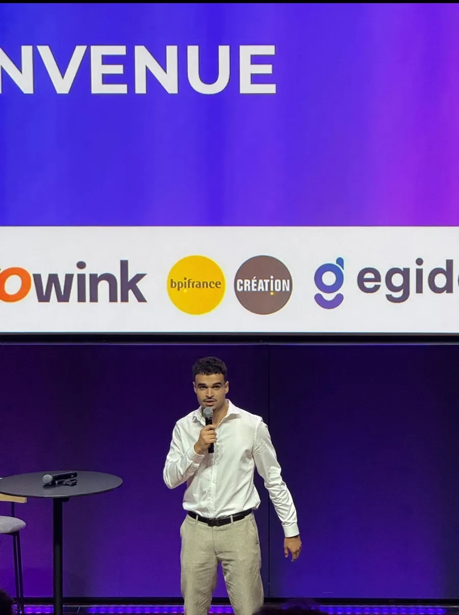 Présentation de SYNCRO sur scène, micro en main, devant un écran violet