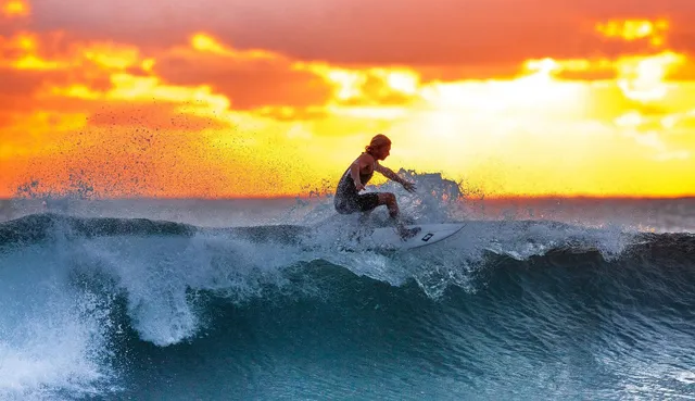 Un surfeur sur la crête d'une vague, devant un coucher de soleil orange